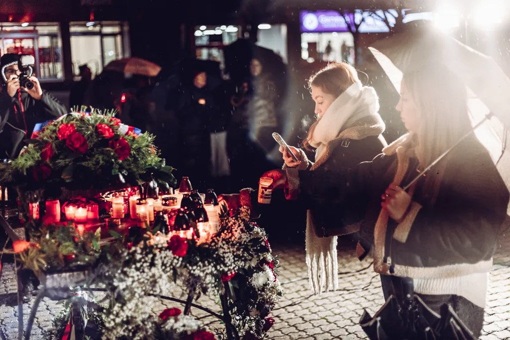 Účastnice zapalují svíčky u pietního místa s věnci.